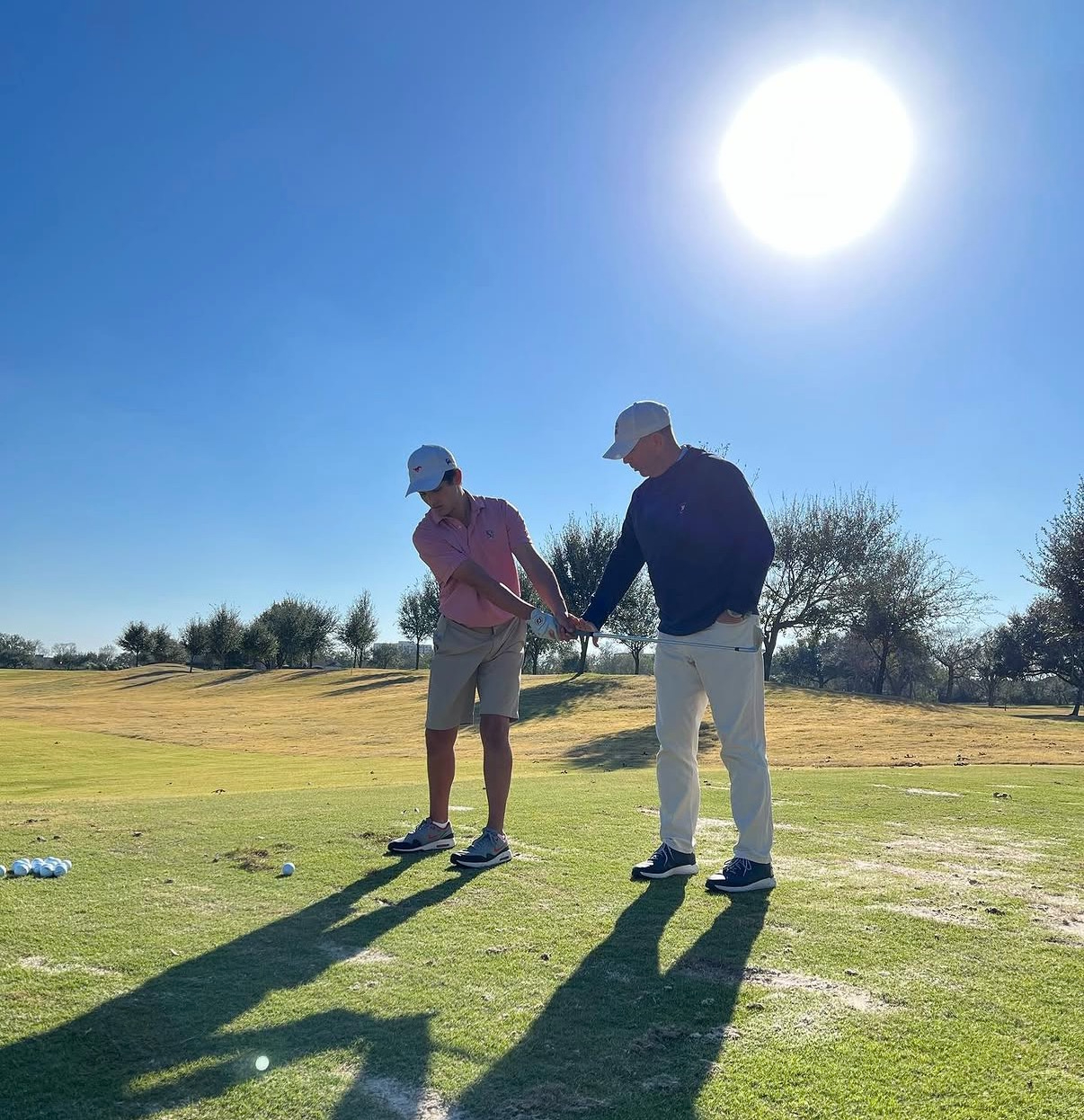Golf coach instructing student on driving range with bright sun